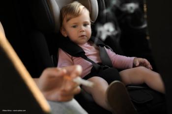 A very young child sits in a car seat while an adult smokes a cigarette near them. Concept image for secondhand smoke, exposure to smoking and early onset myopia development and progression in children. Image credit: ©New Africa – stock.adobe.com