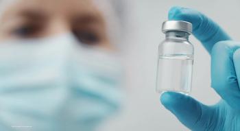 A doctor in a mask holds up a vial of medicine. Image credit: ©MYDAYcontent – stock.adobe.com