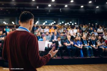 An audience watches a presenter speak at a conference. Image credit: ©Moose – stock.adobe.com