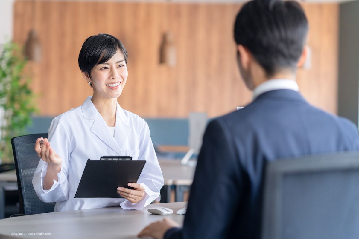 A physician sits at a table with a patient, taking his information on a clipboard. Image credit: ©dai2003 – stock.adobe.com