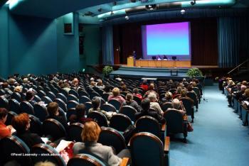 A group of people in an auditorium watch two experts give a presentation. Image credit: ©Pavel Losevsky – stock.adobe.com