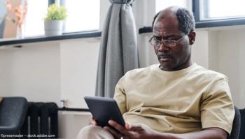 An elderly Black man with glasses sits in a room, reading something on a tablet. Concept image for Black and Hispanic patients with subretinal drusenoid deposits and age-related macular degeneration (AMD). Image credit: ©pressmaster – stock.adobe.com