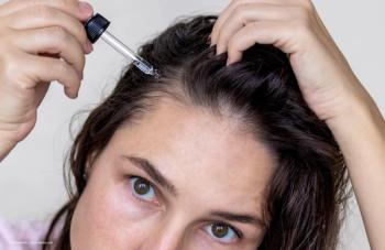 A woman applies a topical hair treatment to her hair roots. Image credit: ©Alexandra – stock.adobe.com