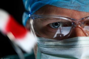 A close-up of a doctor's face. The doctor wears PPE including a mask and safety goggles. Oncology and ophthalmology concept image. Image credit: ©H_Ko – stock.adobe.com