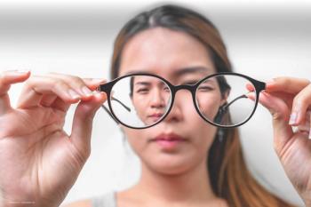 A woman with myopia holds a pair of glasses at a distance and looks through the vision-correcting lens. Paediatric myopia control concept. Image credit: ©Chanintorn.v – stock.adobe.com