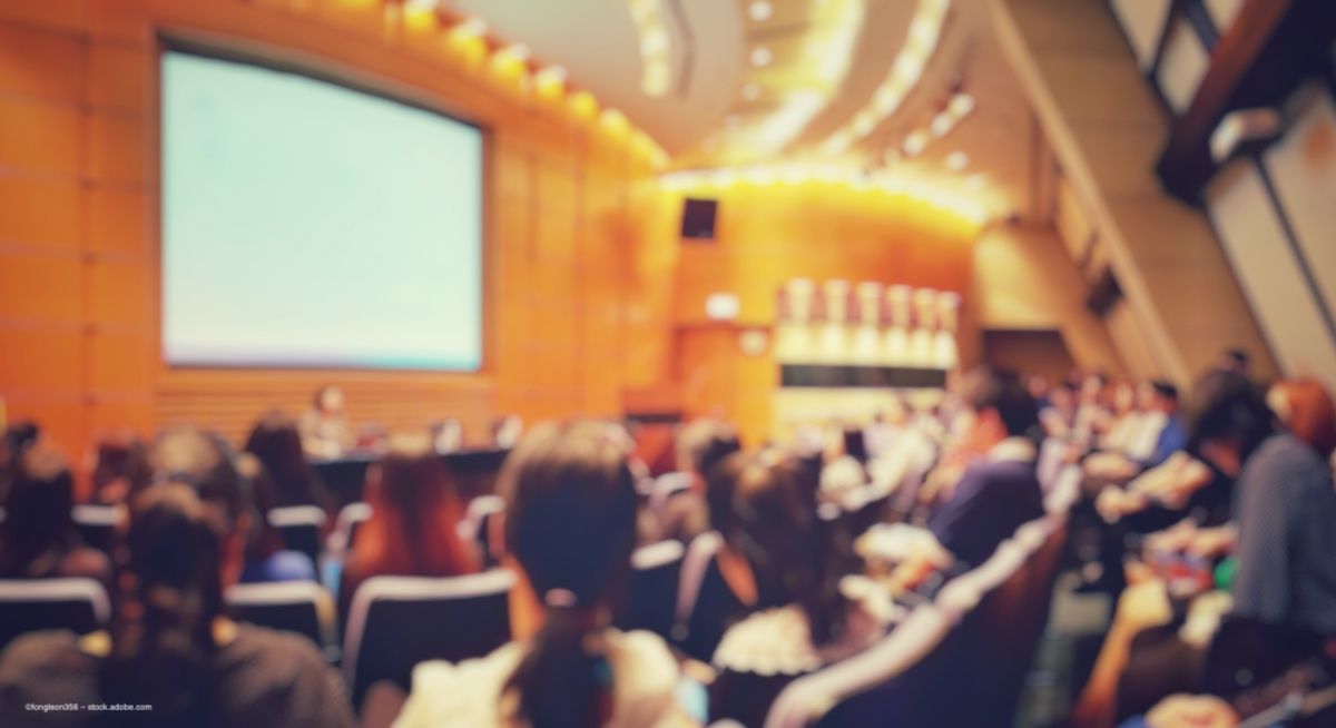A blurred image of an audience in an auditorium where a conference speaker is presenting. Image credit: ©fongleon356 – stock.adobe.com