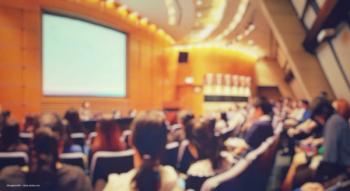 A blurred image of an audience in an auditorium where a conference speaker is presenting. Image credit: ©fongleon356 – stock.adobe.com