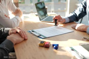 People gather around a desk as a document is stamped for approval. Image credit: ©88studio – stock.adobe.com