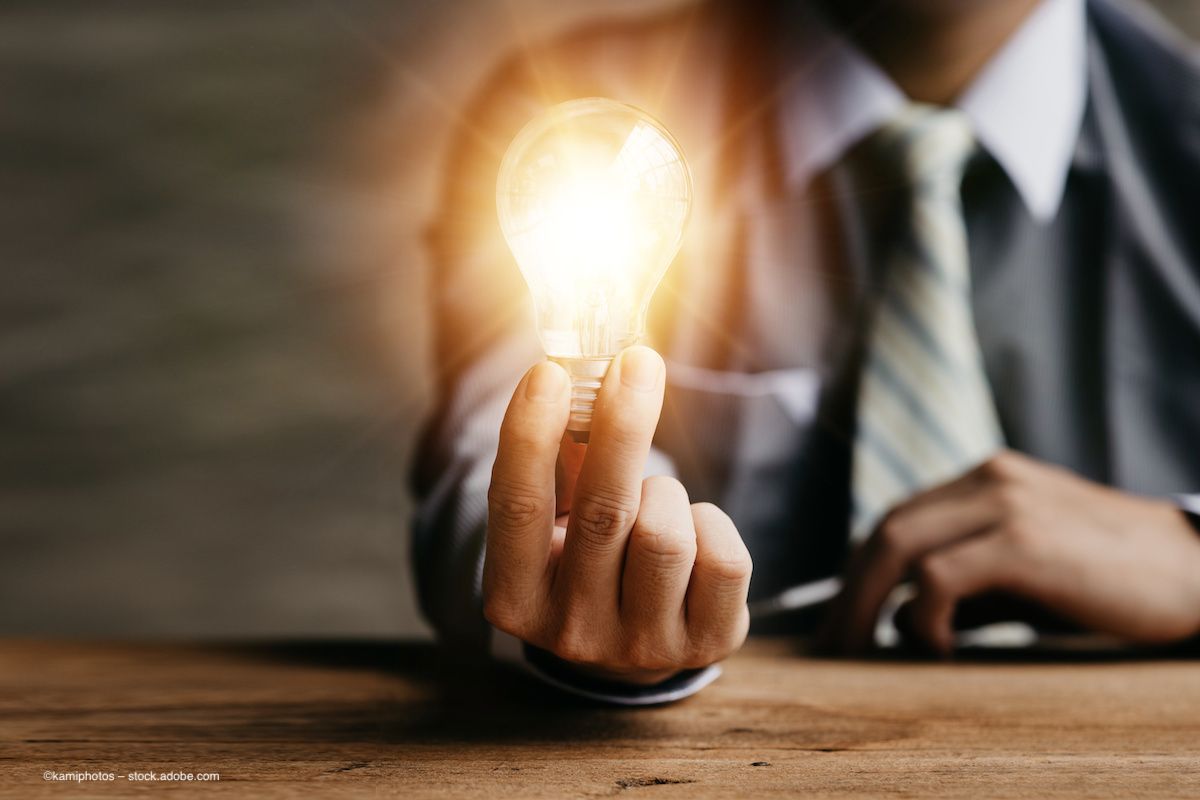 A person in a business suit holds a lit-up lightbulb. Image credit: ©kamiphotos – stock.adobe.com