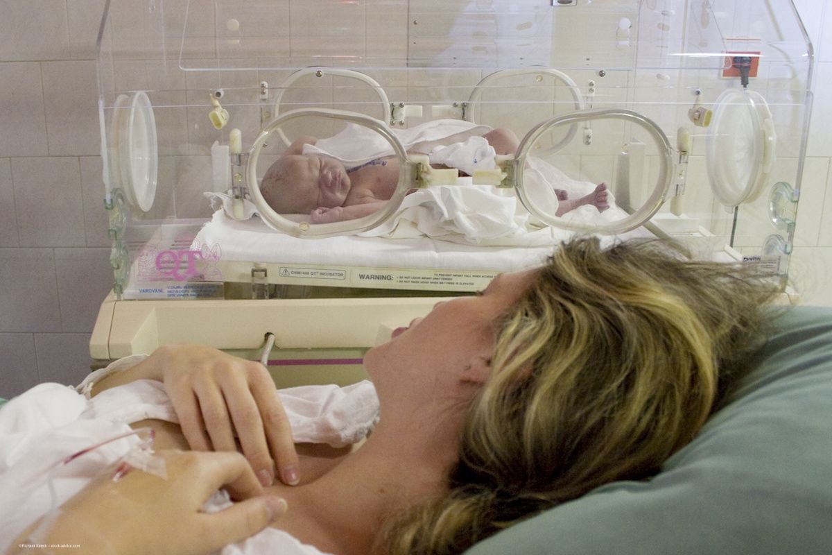A mother who has recently given birth looks at her baby, who rests in an incubator. Image credit: ©Richard Semik – stock.adobe.com
