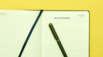 A green notebook with "AAO 2024 schedule" written on the top of the page. A matching green pen rests on the notebook. Image credit: ©AndErsoN – stock.adobe.com