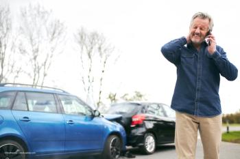 A man is on the phone next to the aftermath of a car accident. Image credit: ©Southworks – stock.adobe.com