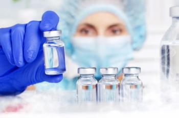 A medical professional in latex gloves and personal protective equipment reaches into a refrigerator to access vials. Image credit: ©Mikhailov Studio – stock.adobe.com