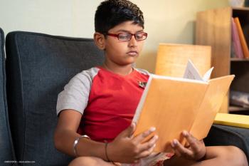 A young boy with glasses reading a book. Concept image for atropine drop paediatric myopia treatment approval in India. Image credit: ©WESTOCK – stock.adobe.com
