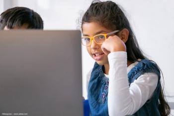 A young girl wearing glasses looks at a laptop, perhaps while attending online school. Concept image for COVID-19 and paediatric astigmatism. Image credit: ©Mangostar – stock.adobe.com