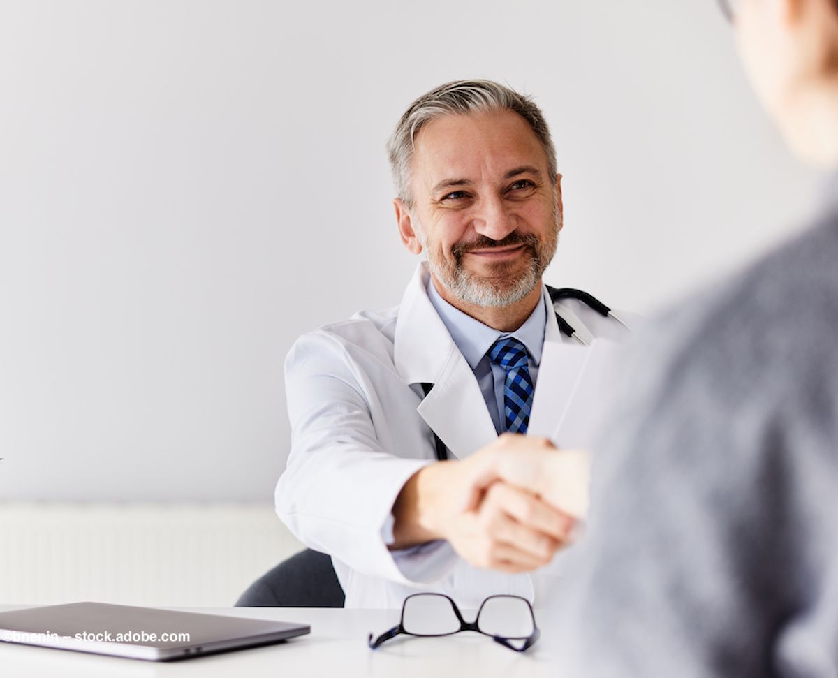 A doctor in a white coat shakes hands with someone off-screen. Image credit: ©bnenin – stock.adobe.com