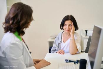 A patient with a pained expression touches her temple, while a female physician looks at her in an office setting. Image credit: ©Svitlana – stock.adobe.com