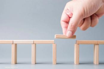 A bridge made from building blocks has an incomplete area. A hand reaches down with the missing block to close the gap. Concept image for age-related macular degeneration therapy and treatment article, IOL implantation and ophthalmology. Image credit: ©patpitchaya – stock.adobe.com