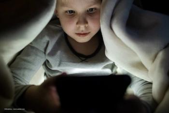 A child under a blanket scrolls on a cell phone. Concept image for phone use, short form content, TikTok, Instagram, ocular pathologies and eye health. Image credit: ©Siniehina – stock.adobe.com