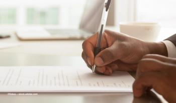 A hand signs a contract on a table. Image credit: ©fizkes – stock.adobe.com