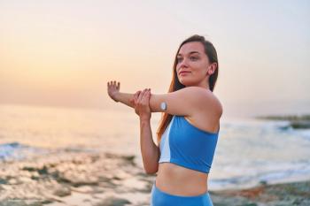 A woman on a beach stretches. She has a sensor/port on her arm for insulin checking, implying she has diabetes. Concept image for diabetes and diabetic retinopathy. Image credit: ©Goffkein – stock.adobe.com