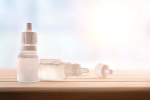 Vials of eye drops sitting on wood top table