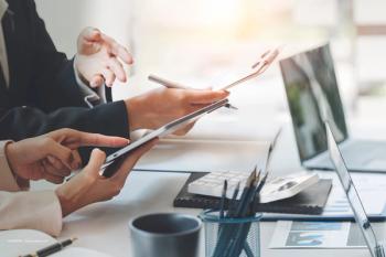 Two people sit at a table. Their hands are visible, as are computers, pencils, notebooks, clipboards and documents. Concept image for business merger, licensing partnership, work collaboration, commercialisation throughout Europe, Re-Vana Therapeutics and Boehringer Ingelheim ocular eye drug therapy.  Image credit: ©NAMPIX – stock.adobe.com
