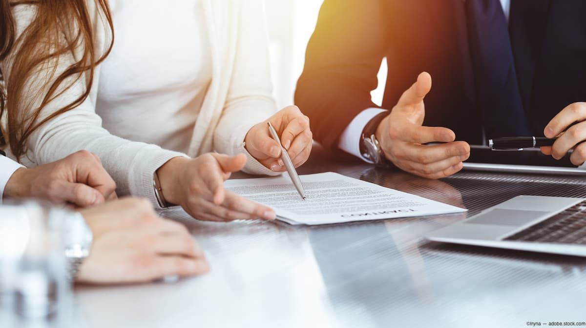 Business employees signing document at table Image credit: AdobeStock/Iryna