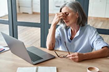 Older woman holding bridge of nose at desk Image credit: AdobeStock/insta_photos