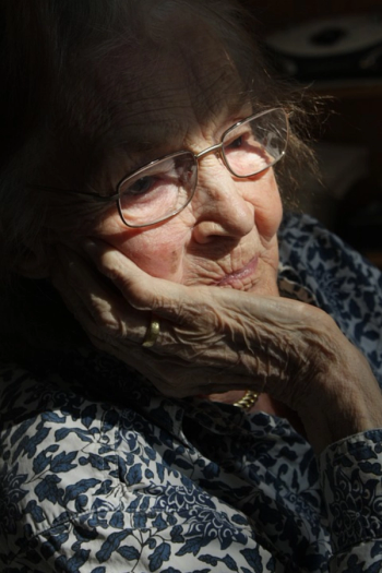 an elderly woman rests her face with glasses on hand