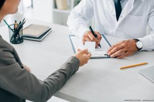 Patient handing doctor with clipboard an insurance card Image credit: AdobeStock/LIGHTFIELDSTUDIOS