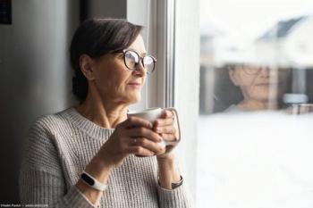 Older woman holding cup looking out window Image credit: AdobeStock/VadimPastuh