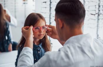Optician puts glasses on young girl Image credit: AdobeStock/standret