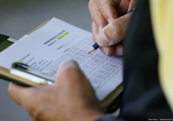 Person filling out scorecard on clipboard. Image credit: AdobeStock/RonAlvey