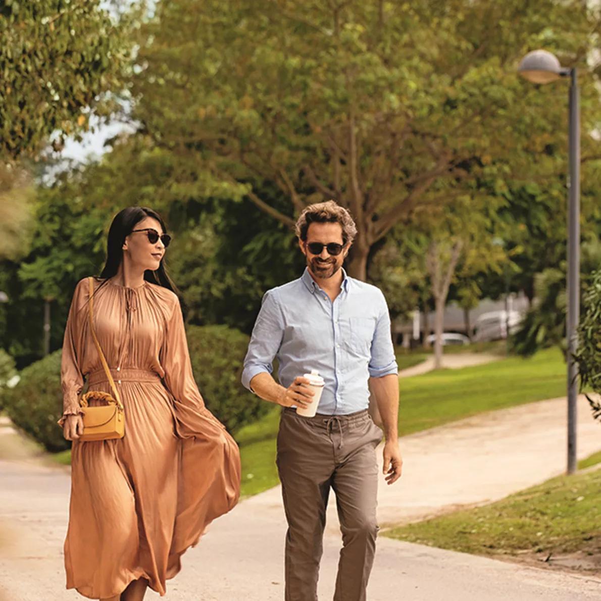 A man and woman walking outside with sunglasses on. Image credit: HOYA Vision Care