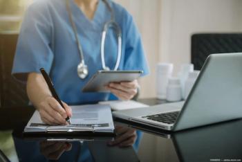 Clinician sitting at desk with tablet, clipboard Image credit: ©NINENII - adobe.stock.com