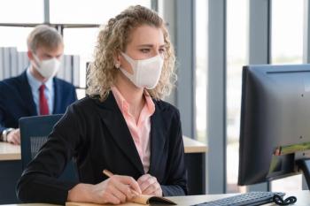 A man and woman work at computers in masks