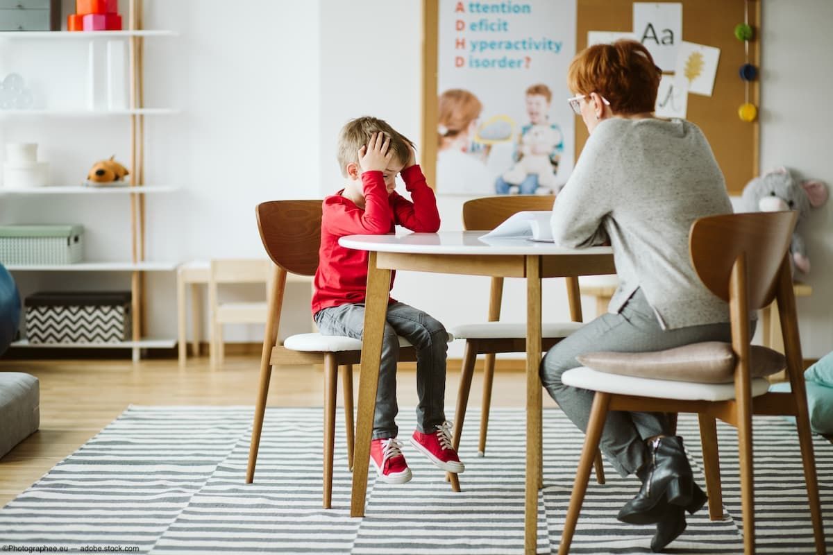 Frustrated child at table with teacher in classroom Image credit: AdobeStock/Photographee.eu