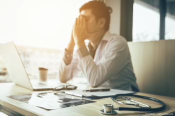 a man cups his face at desk, seemingly from headache