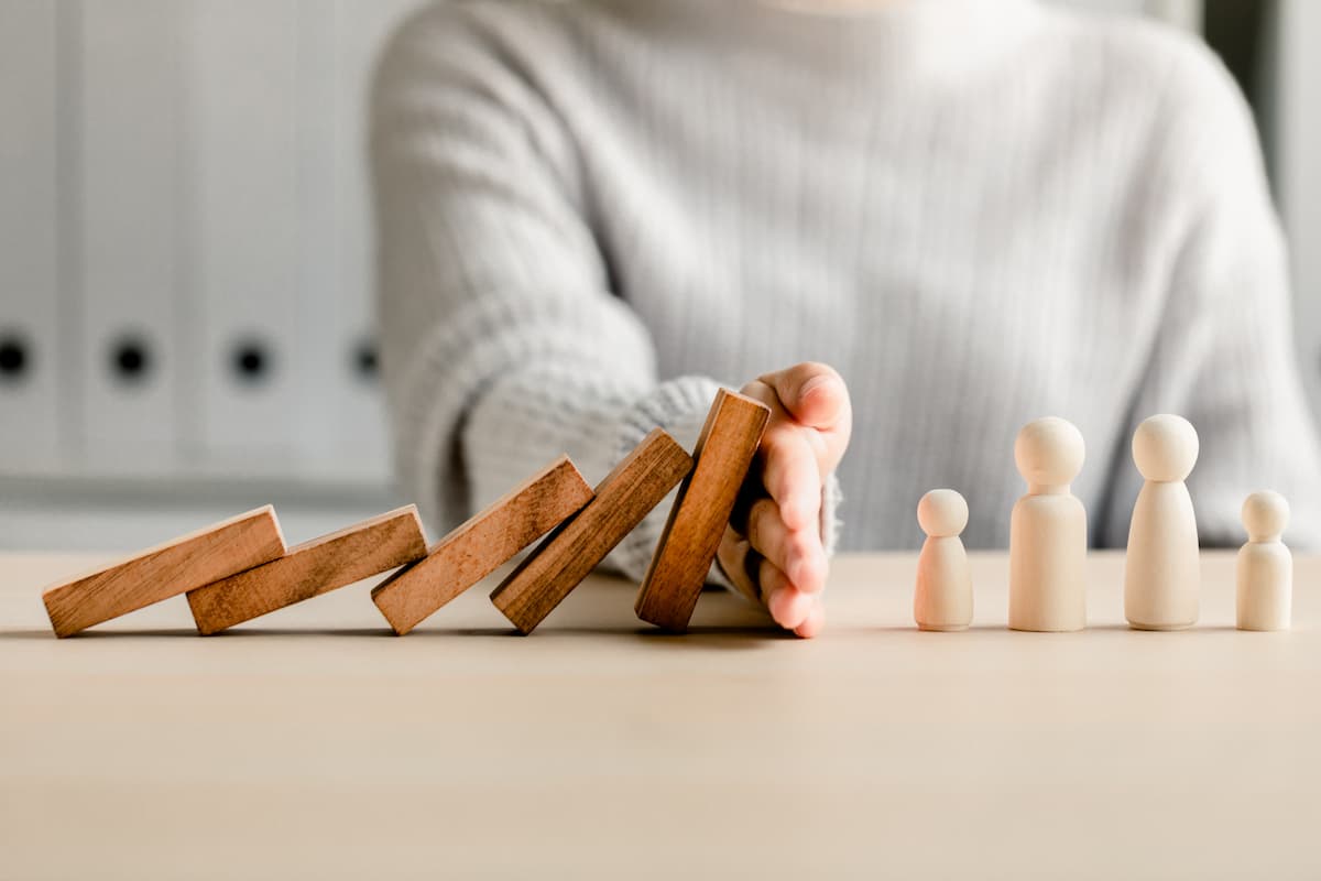 Hand blocking dominos Image credit: AdobeStock/sirichai