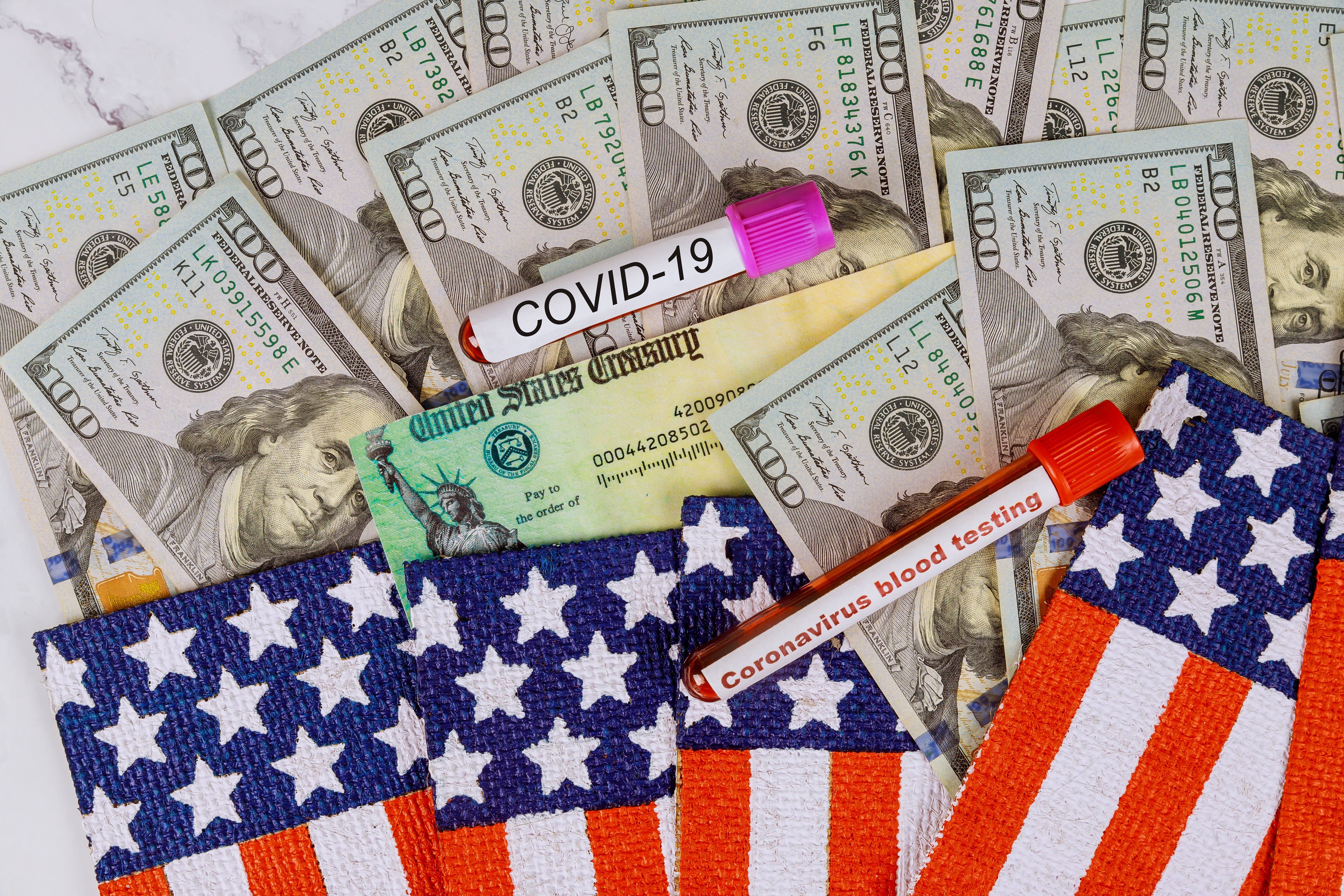 a vile labled covid19 sits atop 20 dollar bills and american flag