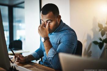 Man with eye strain rubbing eyes at desk Image credit: ©Donson/peopleimages.com 