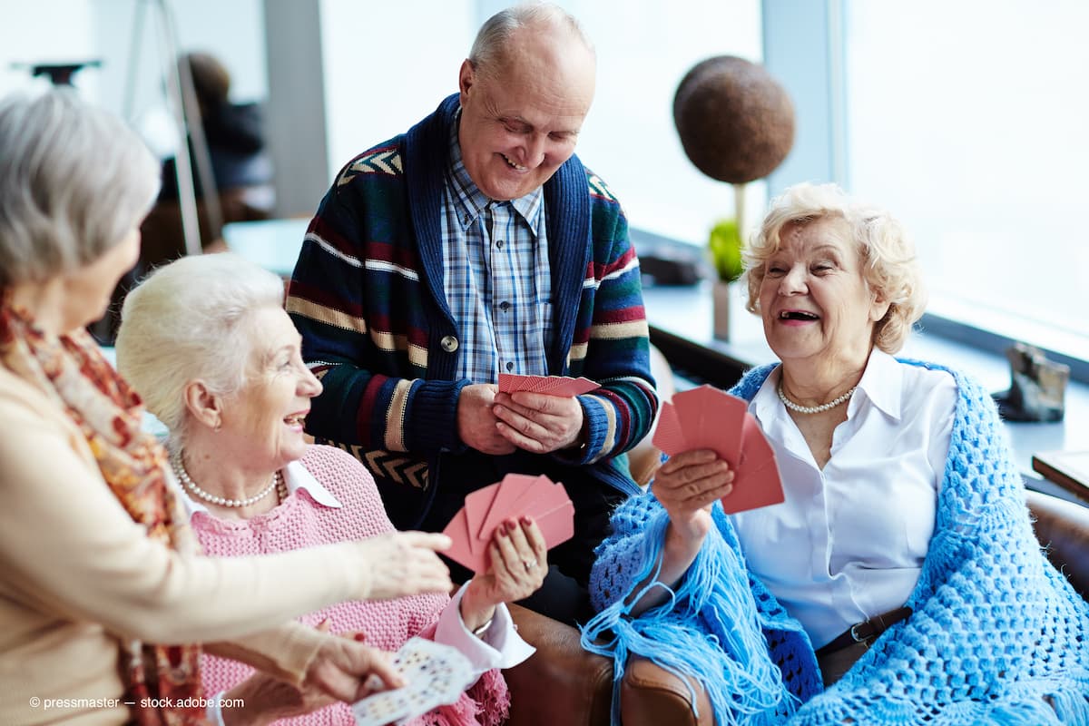 Laughing seniors sitting together playing a card game (Adobe Stock / pressmaster)