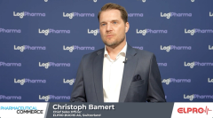 A man with light hair and blue eyes stands in front of a LogiPharma background in a gray suit and white collared shirt