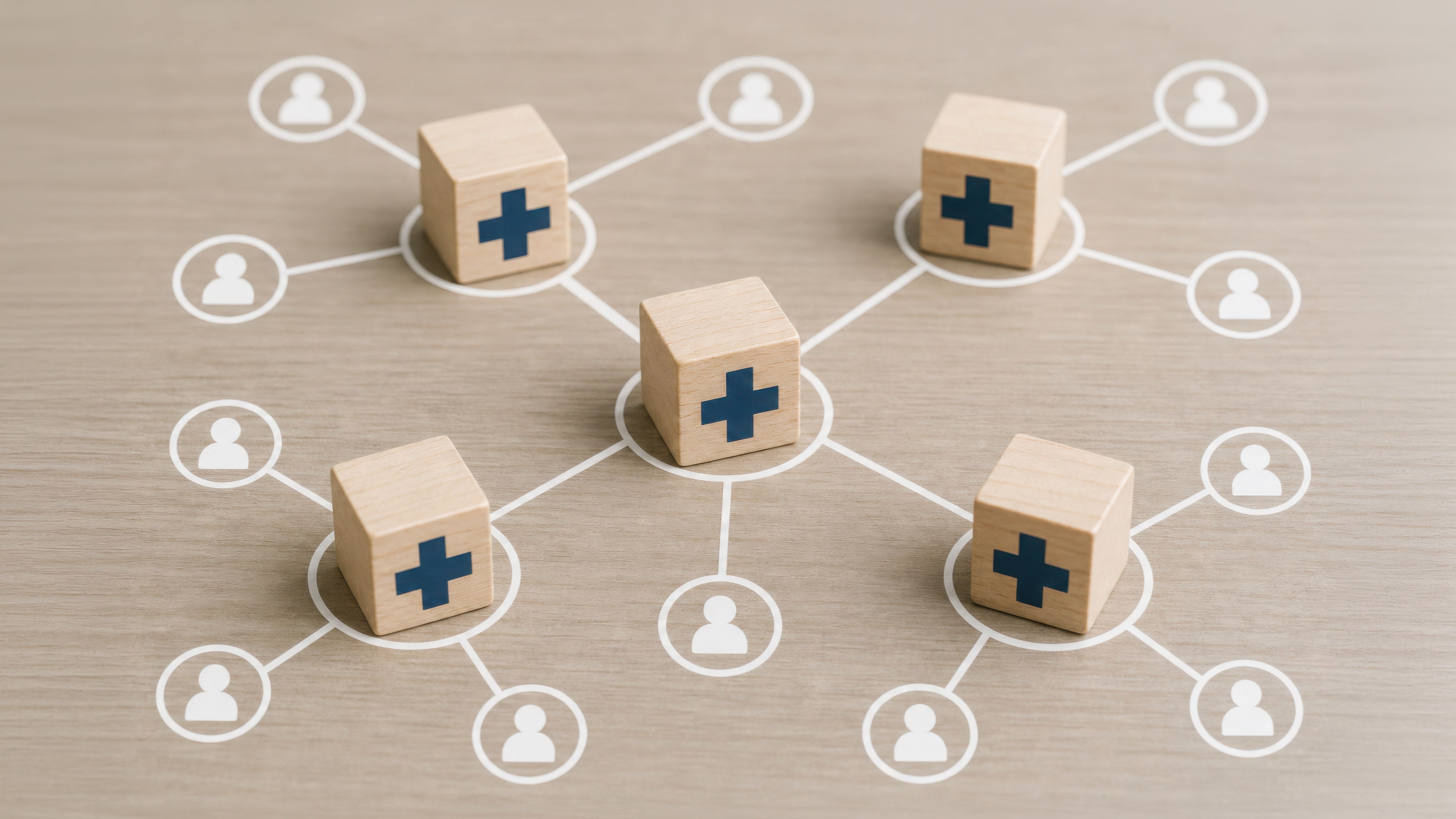 Wooden blocks with medical crosses form a network connecting to people icons, symbolizing a healthcare system, medical distribution, or health insurance network. | © TransPicHub - stock.adobe.com (2014152920)