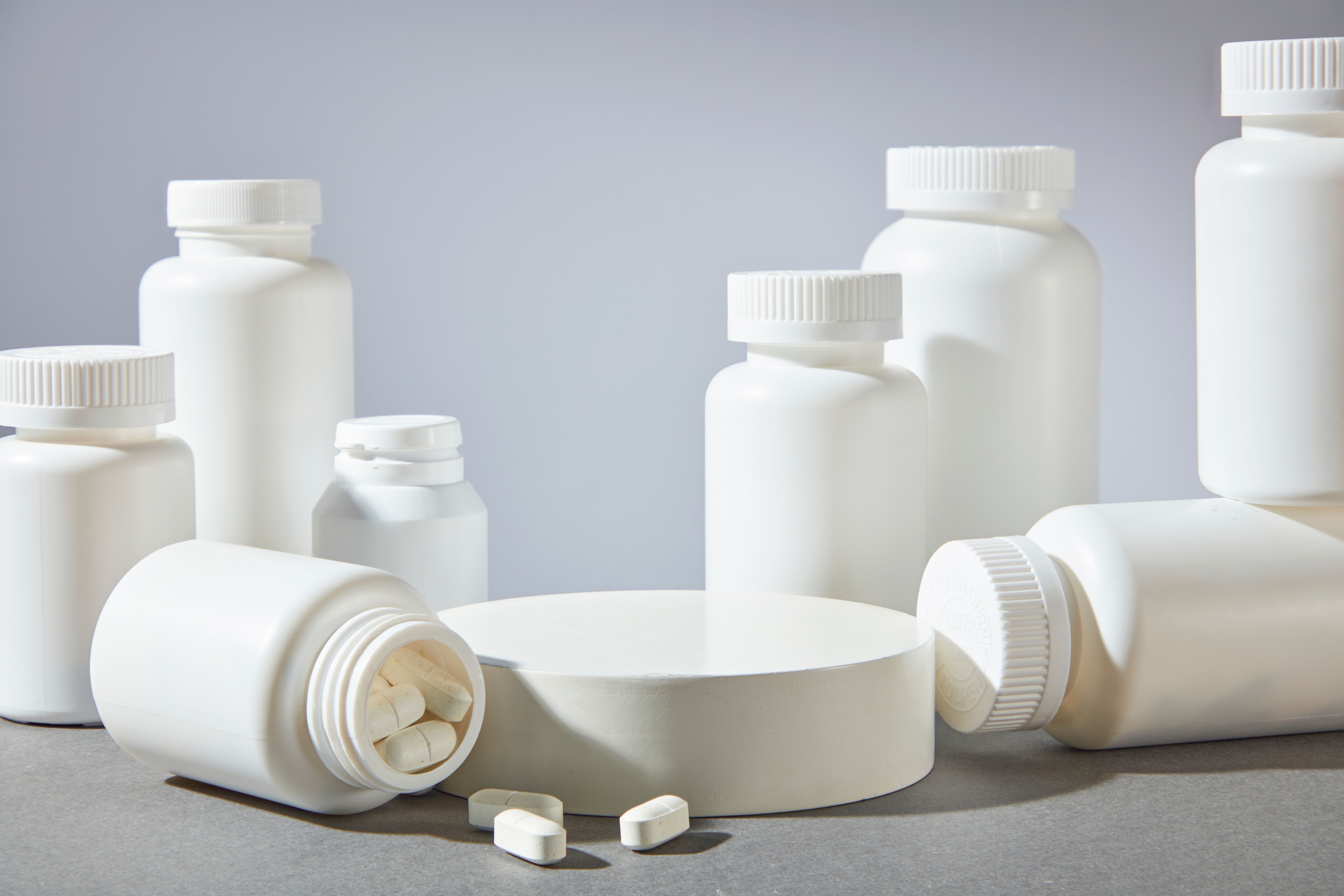 The promotional photo in white minimalism style with plenty white unlabeled medicine bottles surround an empty pedestal in center. Product displaying space, front angle shot | © Tuan Nguyen - stock.adobe.com (911076844)