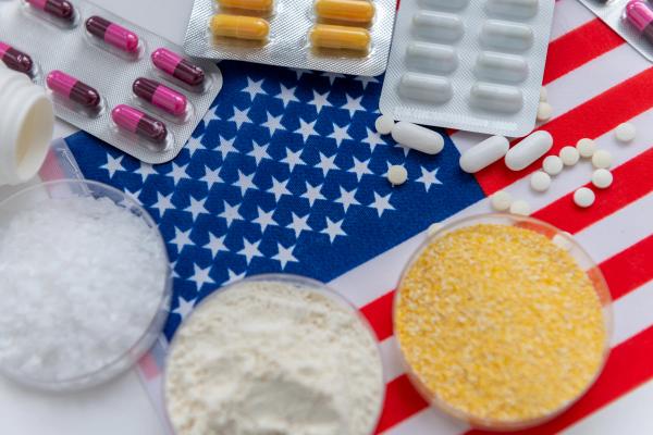 A close up top view of medicine base ingredients in trays, lose medical tablets and packs of capsule on the American flag. An American medicine production, pharmaceutical concept | © Ming - stock.adobe.com (1891331422)