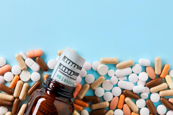 USD dollar bills in a drug bottle over the medical pills. Medicine, healthcare industry and drug trafficking concept. Overhead macro view with copy space - Image credit: Cagkan | stock.adobe.com
