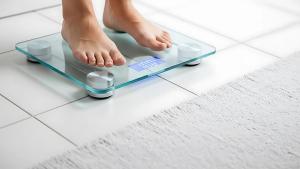 Person's bare feet standing on a digital glass bathroom scale showing weight | Image Credit: Subrata | stock.adobe.com