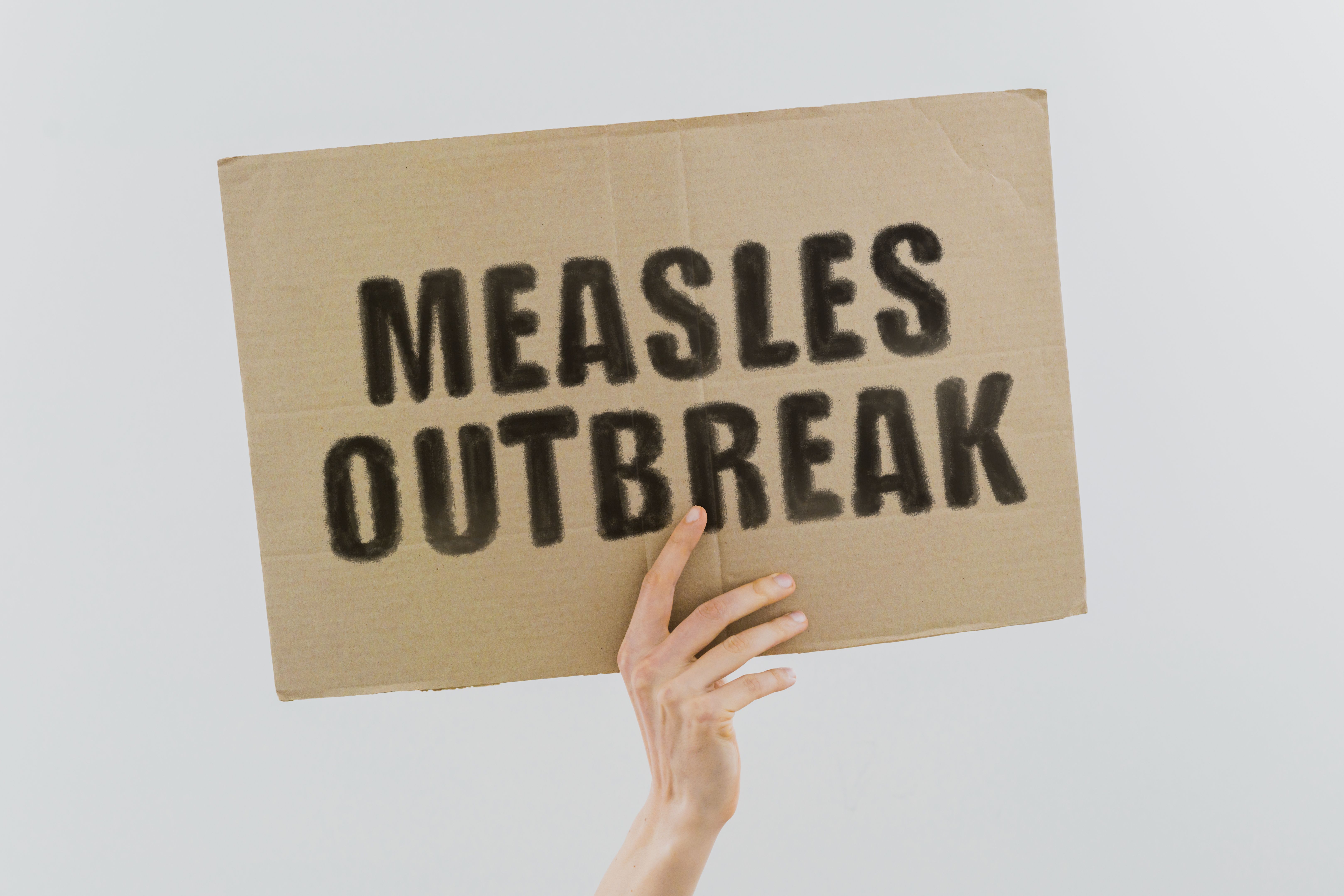Hand holding a banner reading "measles outbreak" | Image Credit: © AndriiKoval - stock.adobe.com